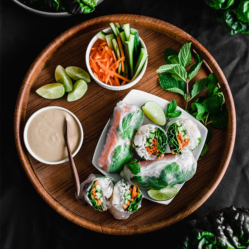 Spring rolls on a fancy charcuterie board, surrounded by various greens and veggies, and a bowl of dip