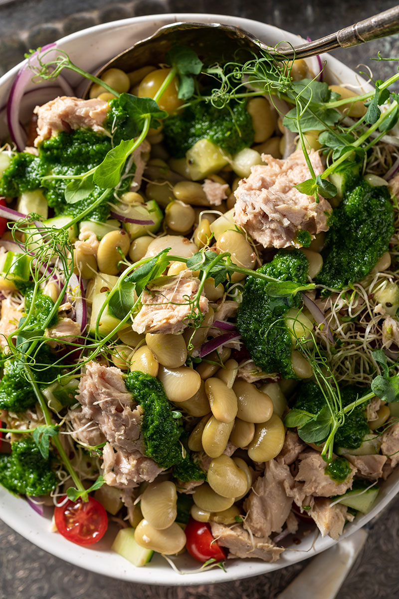 Closeup of a lima bean dish mixed with tuna, cherry tomatoes and herbs/greens.